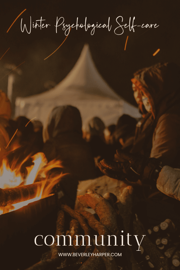 Image of people gathering outdoors in winter. We see the glow of a fire and people warming themselves.
