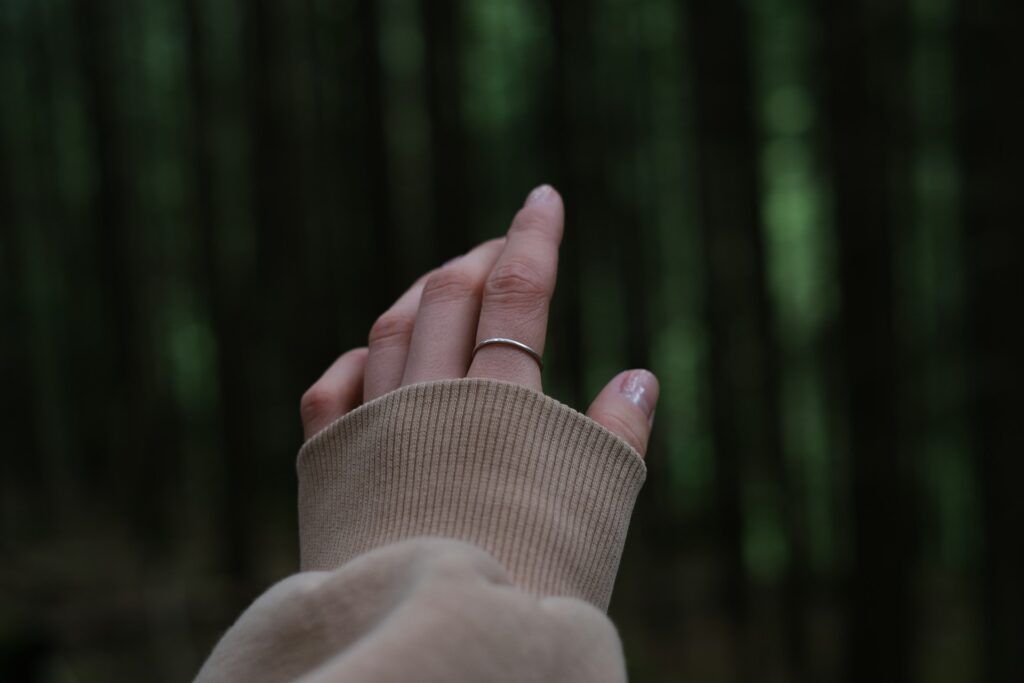 A oman's heand reaches out towards greenery ina forest.