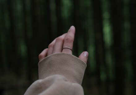 A oman's heand reaches out towards greenery ina forest.
